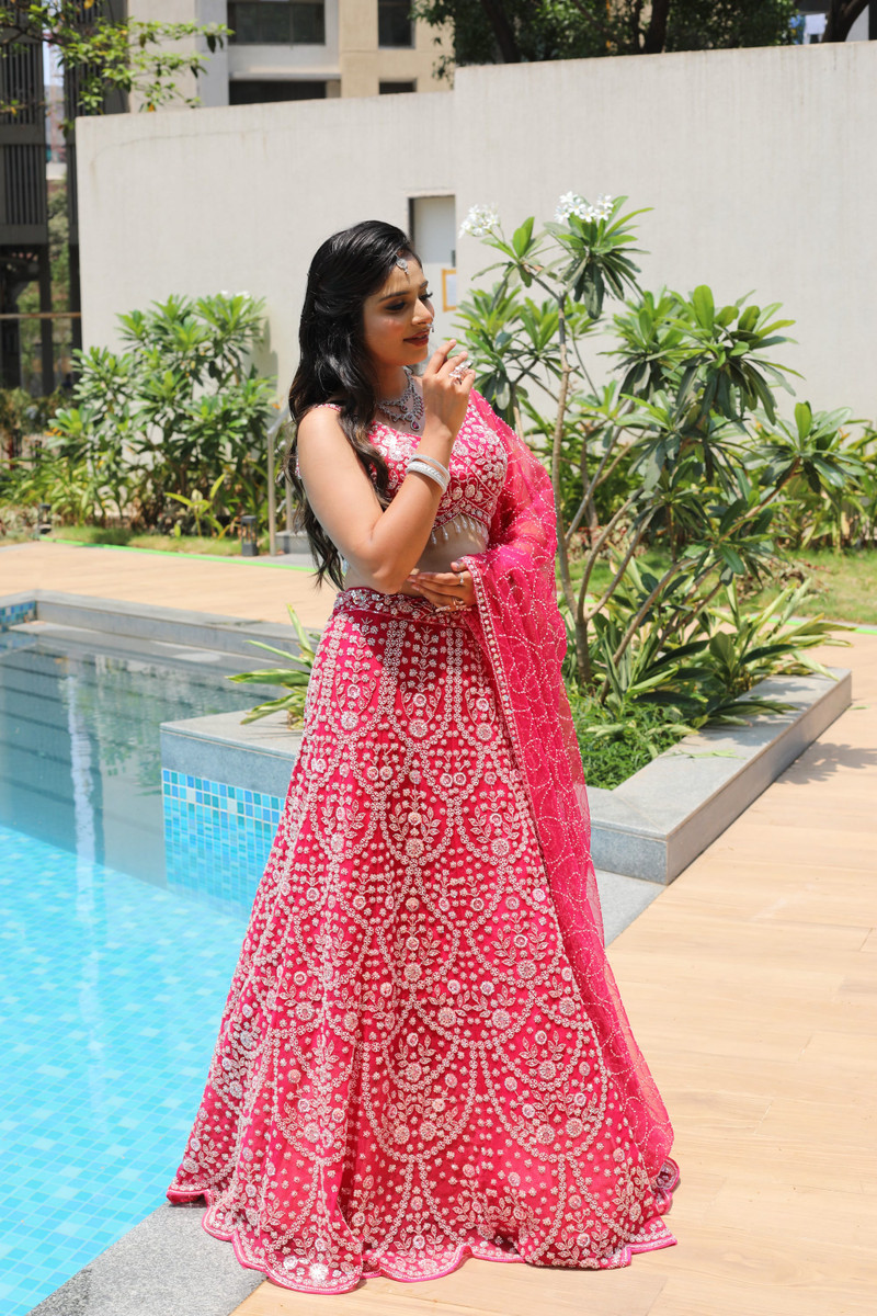 A rani pink lehenga with a sheer dupatta by a pool.