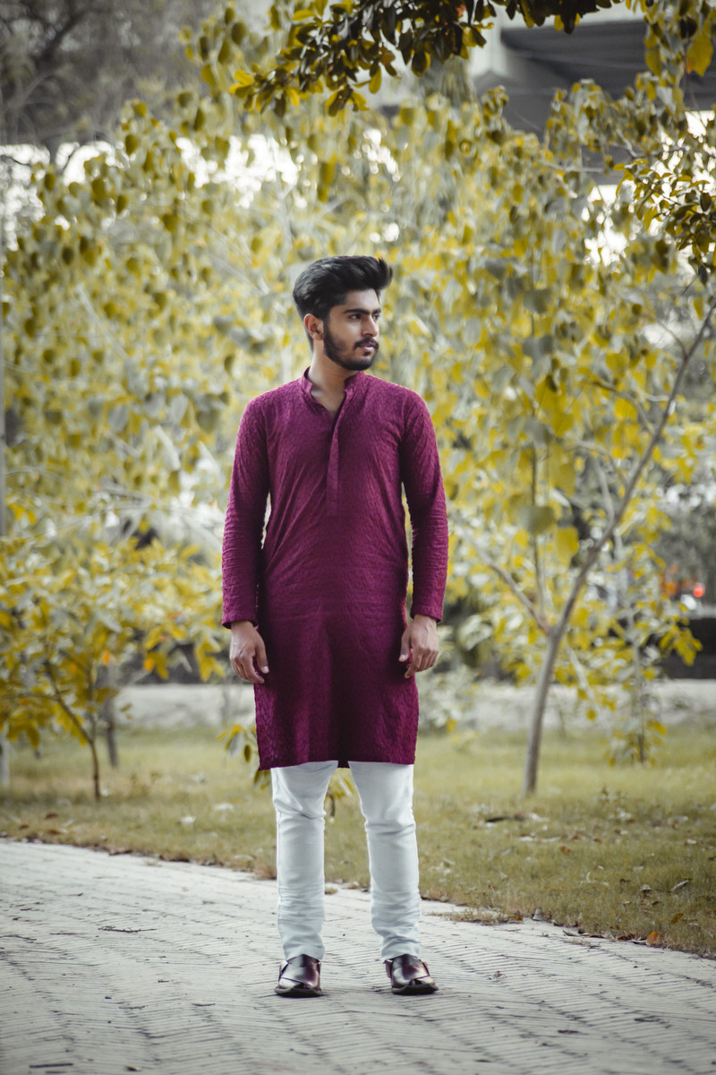 A maroon kurta with white pyjamas on a leafy path.