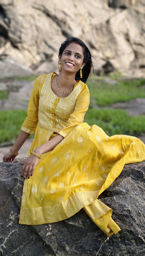 A mustard anarkali with a gold butti, seated on a rock.