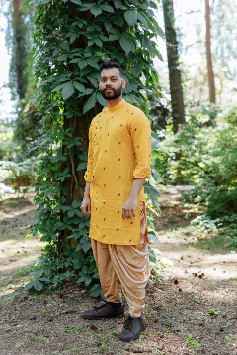 A mustard kurta with dhoti pants beside a tree.