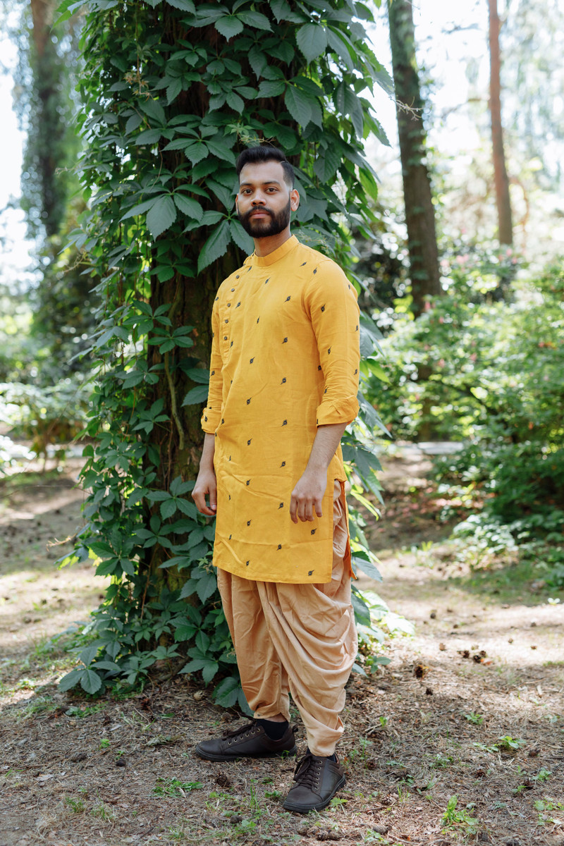 A mustard kurta with dhoti pants beside a tree.