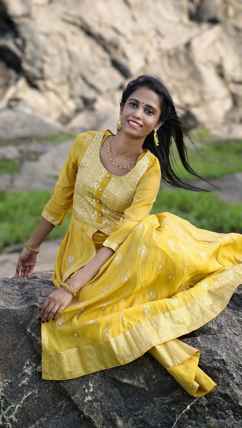 The mustard anarkali, smiling, on the rocks.