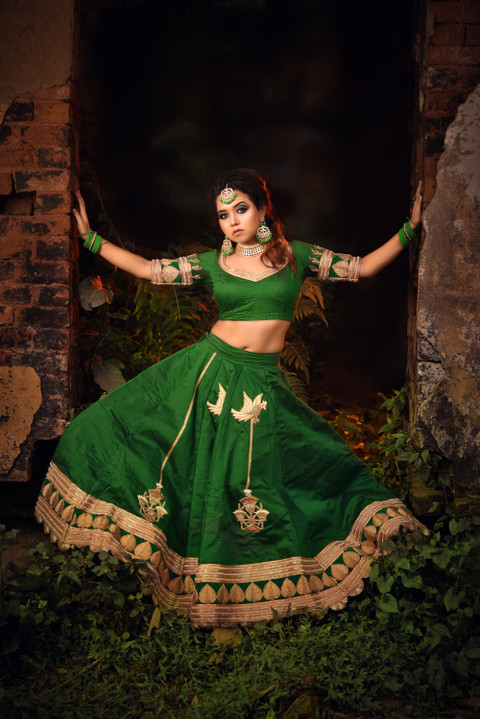 An emerald lehenga with a gold border in an old courtyard.
