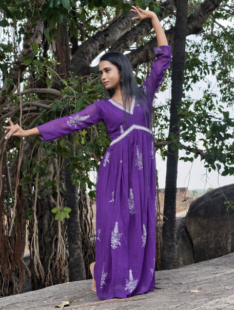 A violet anarkali with a white tie belt under a banyan tree.