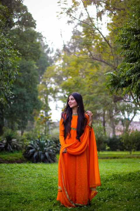 A saffron anarkali with a long dupatta in a garden.
