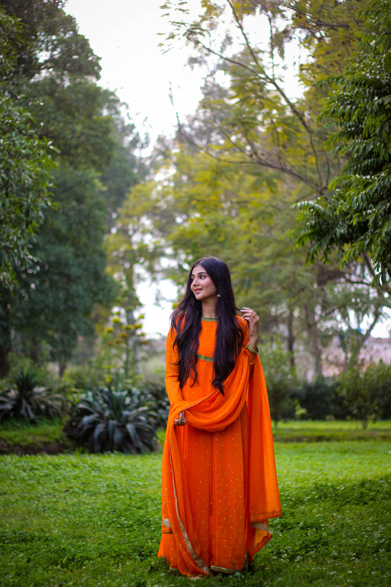 A saffron anarkali with a long dupatta in a garden.