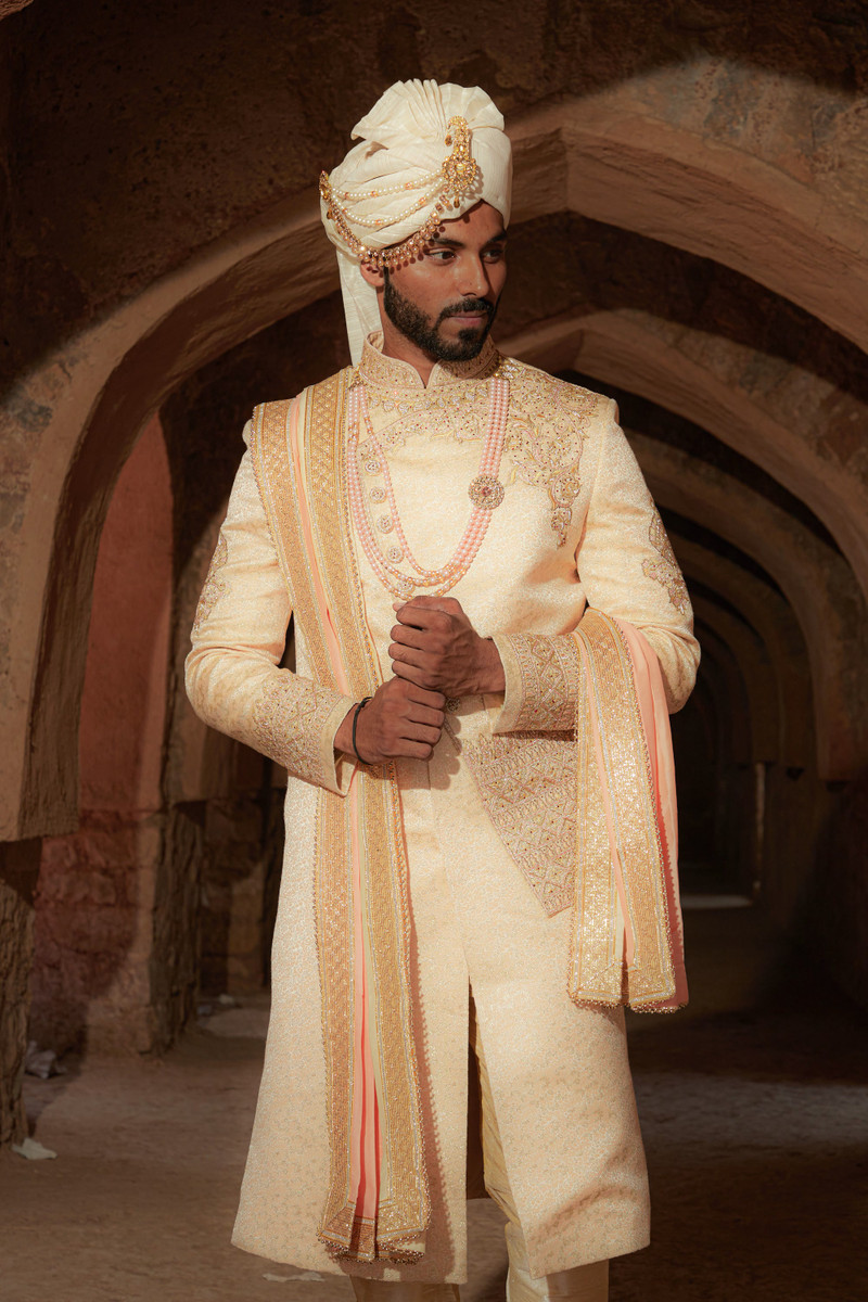 The ivory sherwani under the arches.