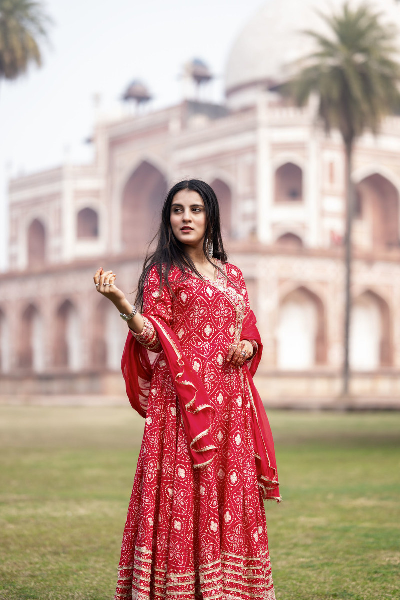 The red bandhani anarkali, standing, the dome behind.